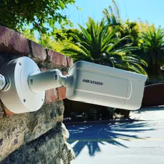 This Hikvision camera is mounted on a brick exterior, providing a clear view of the property entrance. The bright, sunny conditions highlight the camera's ability to produce sharp images in daylight.