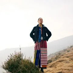 A powerful, heroic pose against the sky. The styling here is about strength and confidence, with the model standing tall in her environment.