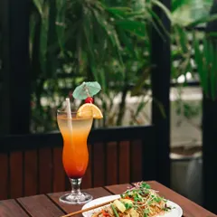 A clean and inviting shot from a restaurant, featuring a colorful cocktail and a plate of noodles, capturing the property's green and modern aesthetic.