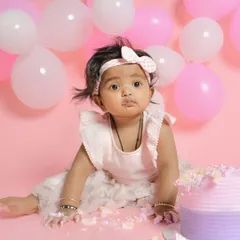 This adorable baby is having a great time during her cake smash session. Her cute expression and cake-covered hands perfectly capture the messy joy of this fun milestone.