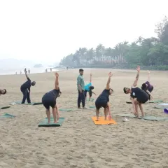 I am guiding my students through a standing spinal twist during a morning beach workshop. This pose helps to increase flexibility in the spine and shoulders while improving balance on the uneven surface of the sand.