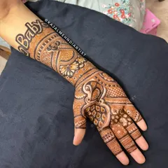 A modern and stylish baby shower design. The word "Baby" is written in a bold, artistic font on the forearm, paired with a detailed peacock and paisley pattern on the hand.