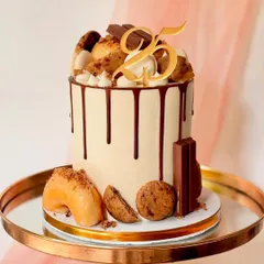 My signature modern drip cake, perfect for a milestone 25th birthday. This tall cake has a smooth buttercream finish, a rich chocolate drip, and is generously topped with donuts, cookies, and chocolate bars.
