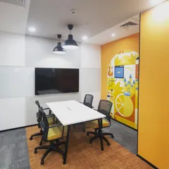 A small, functional meeting room designed for focused collaboration. The space includes a large screen for presentations, a whiteboard wall for ideation, and a colorful mural to keep the creative energy flowing.