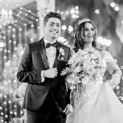A candid black and white shot of Alice and Avi's grand entrance. The image captures their high energy and happiness as they walk in, surrounded by lights and cold pyrotechnics.