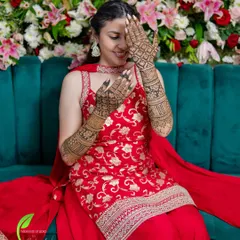 A happy bride posing against a beautiful floral backdrop, her intricate mehendi design adding to her overall look.