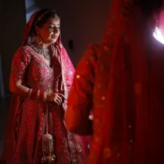A quiet moment of reflection for the bride before her ceremony. The soft lighting highlights the beautiful details of her red lehenga and the subtle glow of her makeup.