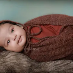 A close up of a swaddled two-month-old baby looking calmly at the camera. These shots focus on their developing features and expressive eyes.