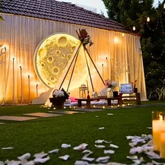 This "Love you to the moon and back" themed setup is perfect for a magical surprise. It features a large, glowing moon backdrop, a cozy teepee for two, and a pathway of scattered petals and candles, all set in a private garden for an unforgettable evening.