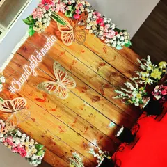 A charming and rustic photo backdrop for an engagement announcement. The wooden panel is decorated with flowers and butterfly cutouts, along with the couple's custom hashtag.