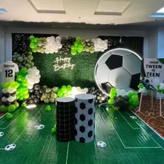 A dream setup for a young football fan. We transformed the space with an artificial grass floor, a giant football backdrop, a 'Happy Birthday' neon sign, and balloon decorations in the team's colors.