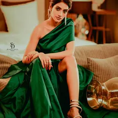 Actress Nusrat Jahan looking elegant in a one-shoulder green satin gown. This full-length shot on a sofa showcases the dramatic silhouette of the dress and her poised, high-fashion pose.