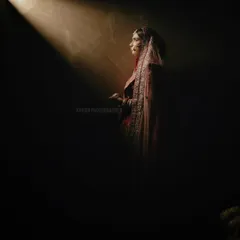 A solitary bridal portrait using dramatic spotlighting. The bride is captured in profile, creating a sense of anticipation and quiet beauty before the ceremony.