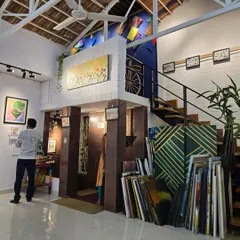 An angled view of the gallery interior, showing the two-level layout with a staircase leading to the mezzanine, surrounded by diverse artworks and neatly stacked canvases.