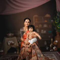A beautiful, painterly portrait of a mother and her baby in a traditional Krishna Janmashtami setup. The rich colors and fabrics create a stunning visual.