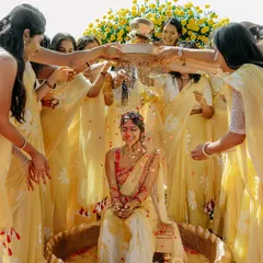 A joyous moment from a Haldi ceremony, with the bride being showered with petals by her bridesmaids in front of a beautiful floral backdrop.