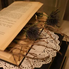 An intimate close-up of dried thistles and twigs placed inside an open book. This highlights our focus on creating unique, small-scale visual moments within a larger event design.