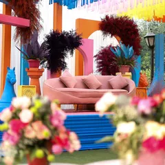 A colorful and eclectic Haldi setup featuring a modern, blush-pink sofa against a backdrop of geometric arches and vibrant tassels. This design combines contemporary furniture with playful, traditional elements for a unique look.