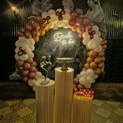 Even in venues with existing decor, I can create a stunning focal point. Here, a 'Bride to be' balloon ring in bronze and white tones stands out against a dramatic wall, with elegant pedestals for the cake and other decorative elements.