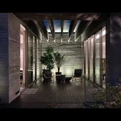 An evening view of a terrace at the Jenga House. The space is framed by exposed concrete walls and wooden ceiling beams, creating an intimate outdoor room that connects directly to the interior.