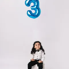 A classic third birthday portrait. The clean white background and the single blue balloon create a simple yet striking image that highlights the birthday boy.