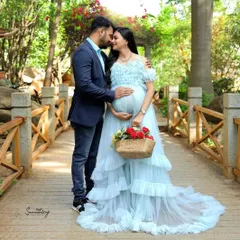 This light blue ruffled gown creates a dreamy, fairytale look, perfect for a romantic couple's maternity shoot. The soft color and delicate ruffles add a touch of elegance, seen here in a beautiful outdoor park setting.
