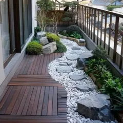 This balcony is transformed into a miniature Japanese-style garden. It features a combination of wooden decking and a dry riverbed of white pebbles, complete with rocks and bonsai-like plants.