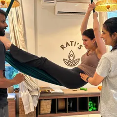 Here, we provide hands-on assistance to ensure everyone feels safe and supported. An instructor helps a student adjust her form in the hammock, ensuring proper alignment for a deeper, more effective stretch.