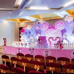 A full stage setup for a grand Minnie Mouse first birthday party. We created a massive Minnie head silhouette with pink balloons as the centerpiece, complemented by themed banners, props, and lighting.