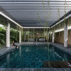 A serene swimming pool with a person dipping their feet in the water, set under a pergola with trailing vines. The space is designed as a peaceful haven, with lush greenery creating a natural screen for privacy.