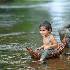 A serene portrait of a young boy sitting peacefully in a wicker boat by the river's edge, surrounded by nature.