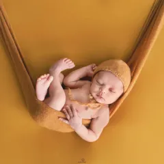 A classic newborn pose, with the baby sleeping peacefully in a mustard-colored sling against a matching backdrop. This highlights the simple, artistic style of my newborn photography.