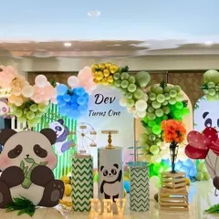 A cute panda theme for a first birthday party. This setup uses large panda cutouts, a multi-colored balloon garland, and custom-wrapped pedestals to match the green and white color scheme.