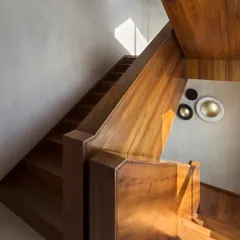 The dog-legged staircase in the House of Terraces is clad entirely in rich Burma teak, serving as a warm, central spine connecting all floors of the villa. The play of sunlight on the wood highlights its natural grain and beauty.