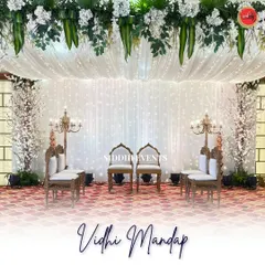 A full view of the pristine white Vidhi Mandap, showcasing the symmetrical arrangement of traditional chairs, candelabras, and cherry blossom trees against a sparkling backdrop.