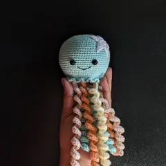 A cute jellyfish amigurumi with a happy smile and long, curly tentacles in pastel colors.