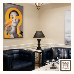 This classic black table lamp, with its carved wooden base, is set in a cozy corner between two deep blue leather armchairs. It provides the perfect ambient lighting for a sophisticated lounge area.
