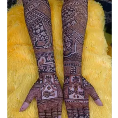 A full-coverage bridal mehndi with a prominent paisley peacock design. The rest of the arm is filled with delicate floral vines and checkerboard patterns, creating a rich and dense look.