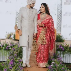 A beautiful couple walking down an aisle lined with purple flowers, against a Sheesh Mahal-inspired backdrop. A picture of timeless elegance.