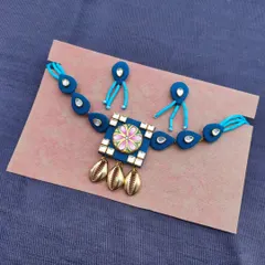 This hand-painted necklace set in blue is a true statement piece. It features a large central pendant with kundan work and kowri shell drops, perfect for a unique ethnic look.