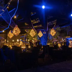 An outdoor Diwali party setting under a canopy of dark fabric and dramatic blue lighting. Multiple crystal chandeliers add a touch of opulence, creating a magical contrast against the night sky.