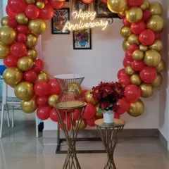 A vibrant red and gold balloon ring setup for an anniversary party at home. The 'Happy Anniversary' neon sign adds a modern touch to this celebratory decoration.