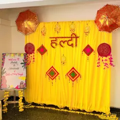 This is a complete Haldi ceremony backdrop package. It includes a vibrant yellow drape background with traditional hangings, a "Haldi" sign, decorative umbrellas, and a custom-painted welcome board for your guests.