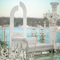 A chic and modern photo seating area set against an ocean backdrop, featuring a white chaise lounge and minimalist white arches.