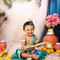 A joyful little Kanha with his flute. The vibrant colors of the costume, peacock feathers, and flowers create a visually stunning portrait.