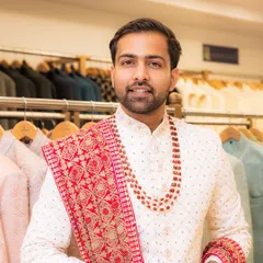 This client looks ready for his wedding day in our classic white sherwani, perfectly complemented by a red beaded mala and a matching embroidered red stole.