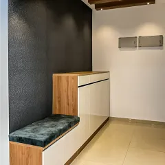 A minimalist foyer with a sleek, low-profile storage unit that includes a cushioned bench. The dark textured accent wall adds depth and sophistication to the clean design.