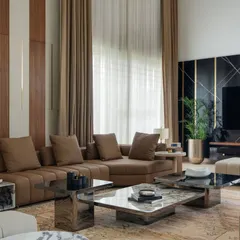 The double-height living area in the Celadon project features a striking black marble wall with brass inlays for the media unit, contrasting with the warm wood paneling. The large sectional sofa and layered coffee tables create a comfortable yet sophisticated space for family gatherings.