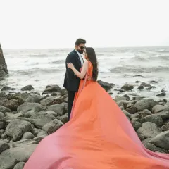 A dramatic shot on a rocky Goa beach, where the bride's vibrant orange gown flows in the wind against the powerful waves, creating a moment of pure cinematic romance.