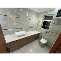 A clean and modern bathroom with a floating vanity and a wall-mounted toilet. The light-colored tiles and gold-toned accents create a bright and elegant space.